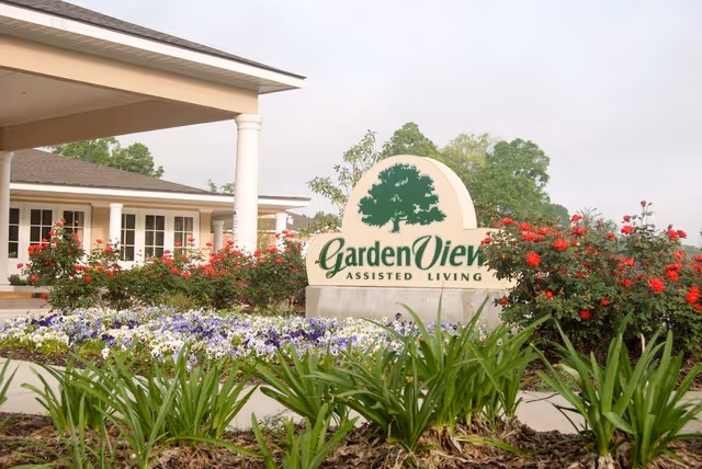 Exterior view of Garden View Assisted Living entrance with sign and blooming flower beds.