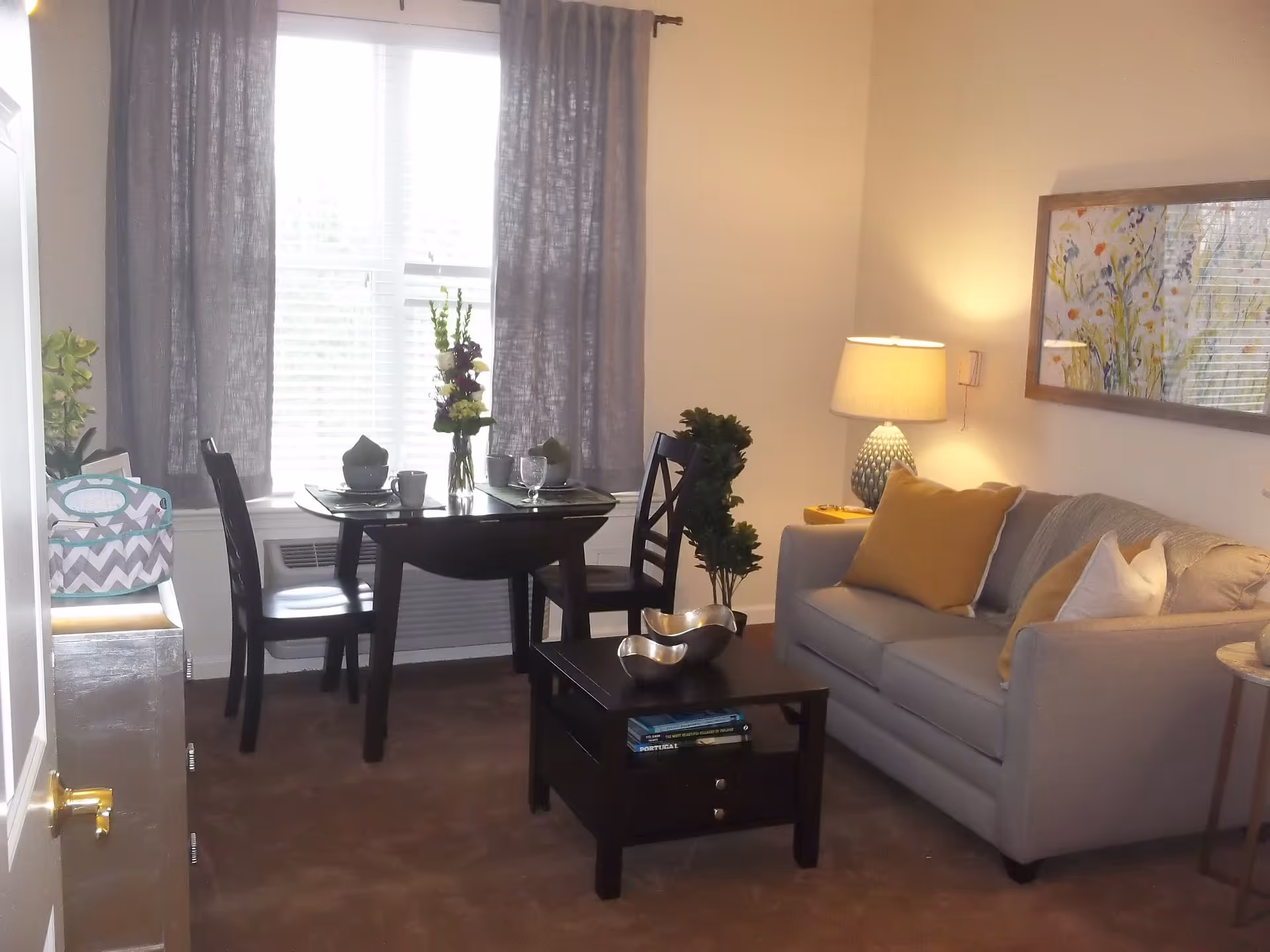 Bright living room with a sofa, coffee table, and a small dining table set by a curtained window.