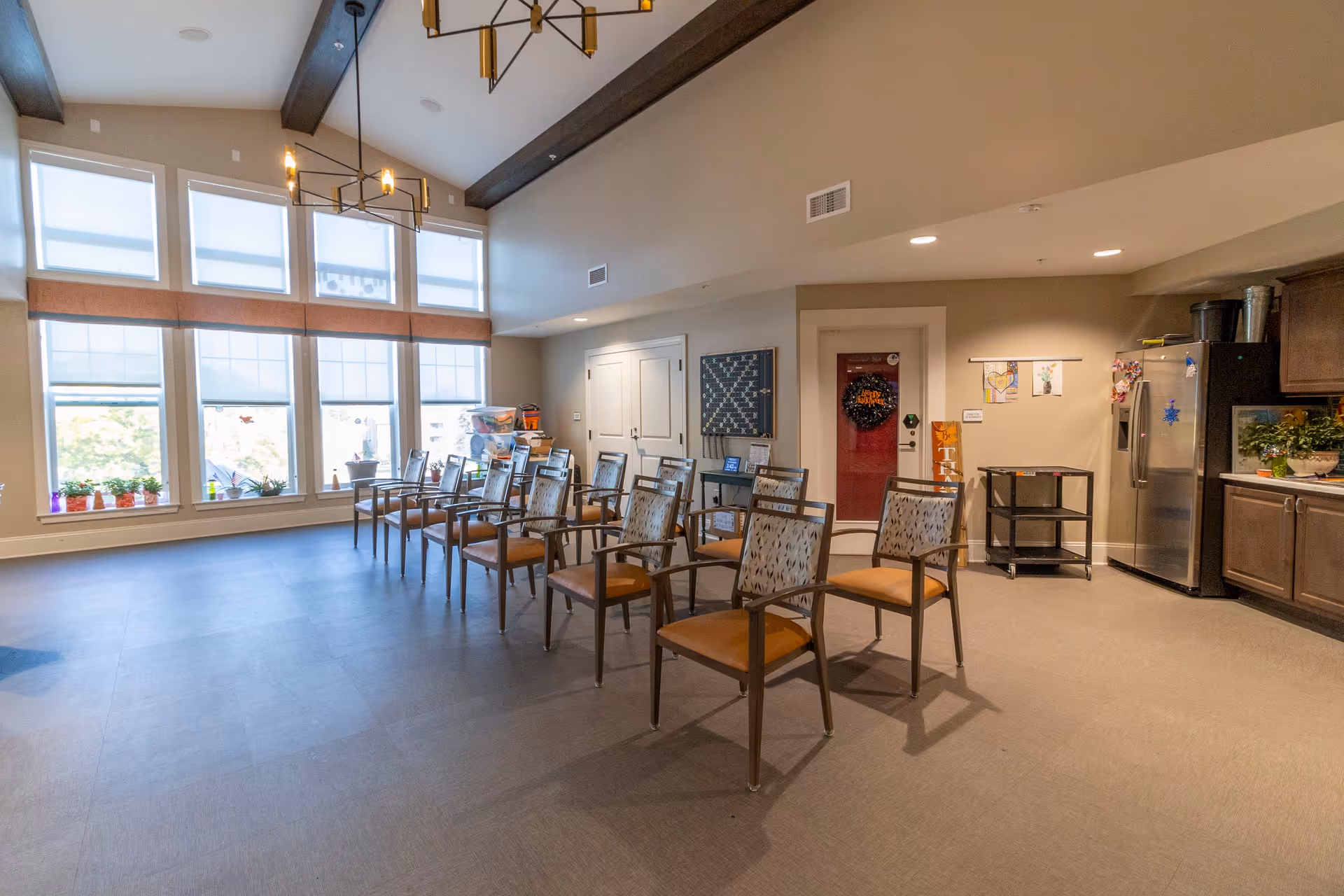 Bright communal activity room with rows of chairs facing large windows and a small kitchenette area.