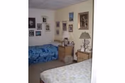 Small furnished bedroom with two twin beds, bedside tables and lamps, and numerous framed pictures on the walls.