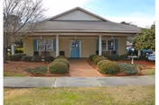 Front view of a single-story beige building with a covered entrance, blue double doors, a walkway and trimmed shrubs.