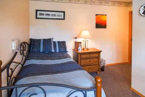 A cozy bedroom with a metal bed, nightstand, lamp, and framed wall art.