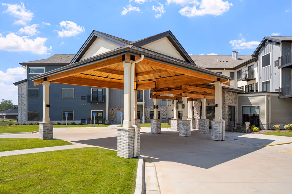 Modern senior living facility exterior with a wooden covered entrance and stone pillars.