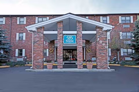 Red brick senior living facility entrance with a blue sign reading The Harrison.