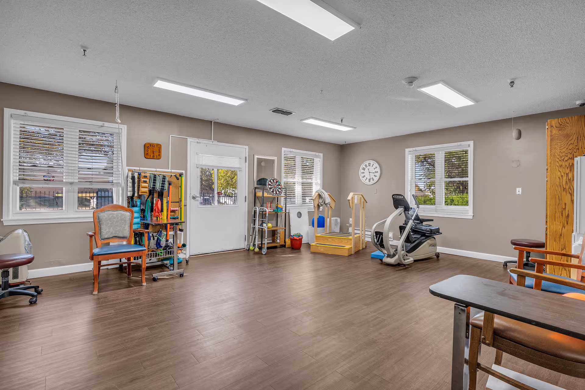 A bright rehabilitation/exercise room with chairs, therapy equipment, exercise bike and windows.