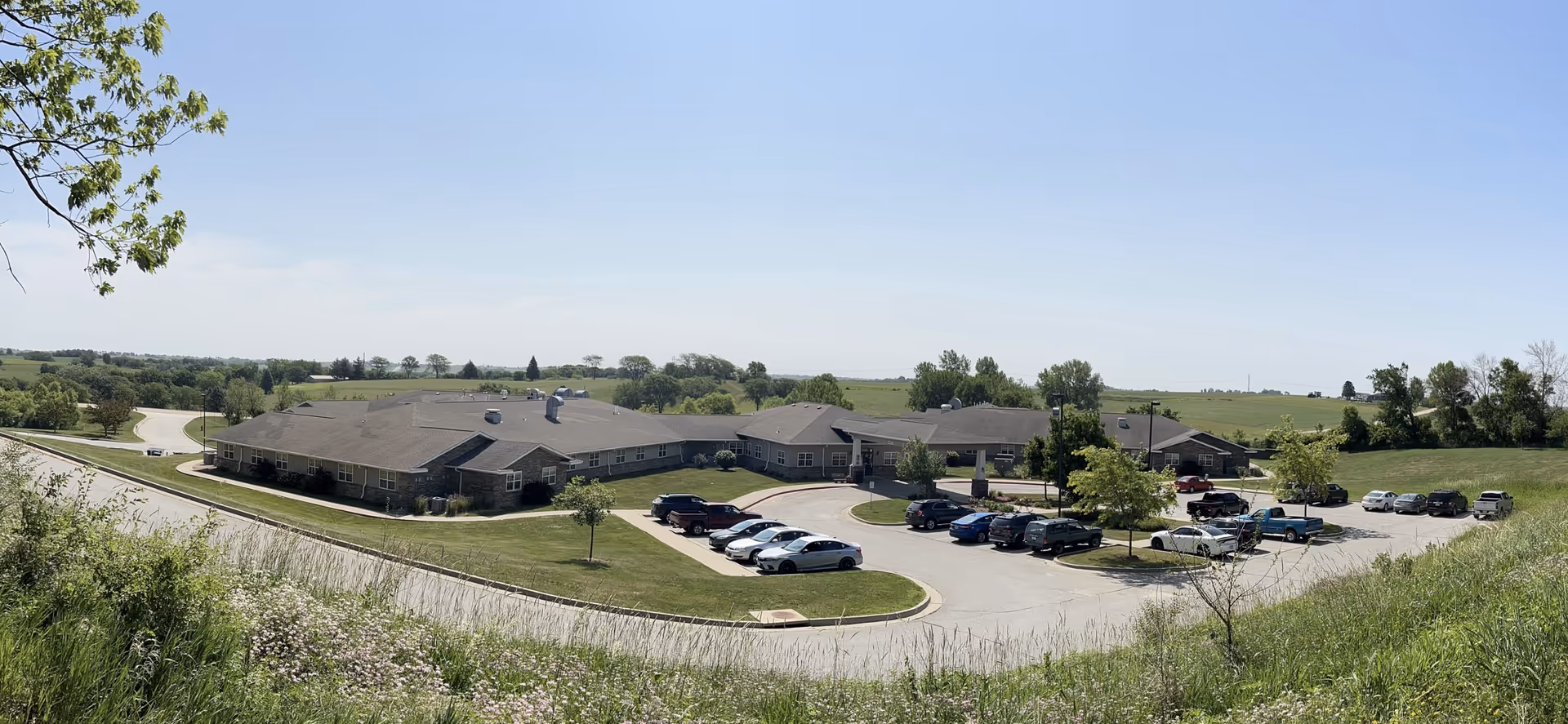 Panoramic exterior view of a single-story senior living facility with a parking lot and grassy surroundings.
