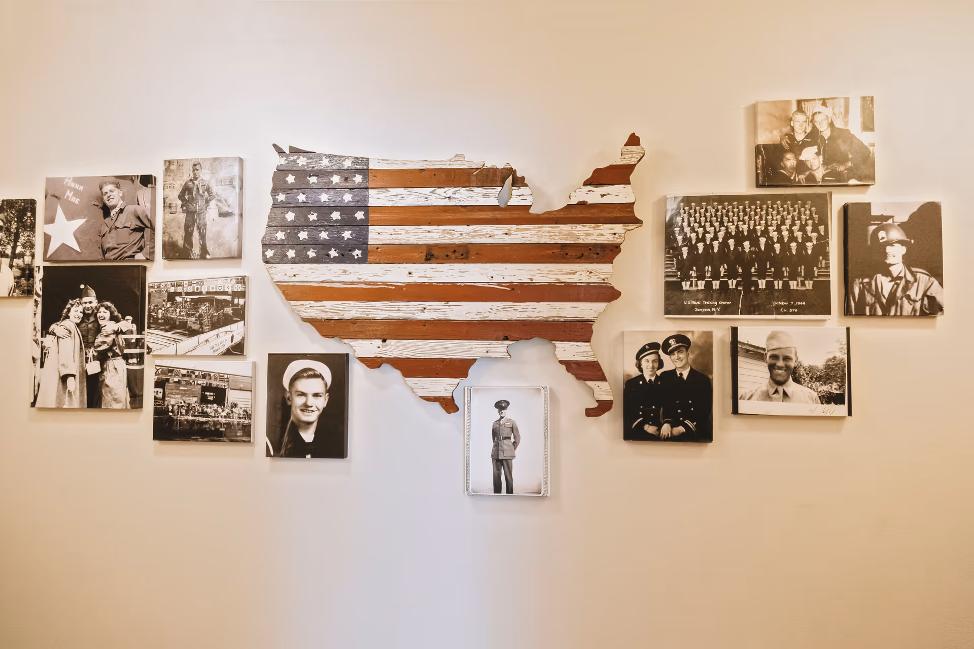 A wall display featuring a wooden cutout of the United States painted with the American flag, surrounded by black and white vintage photographs of military personnel and groups.