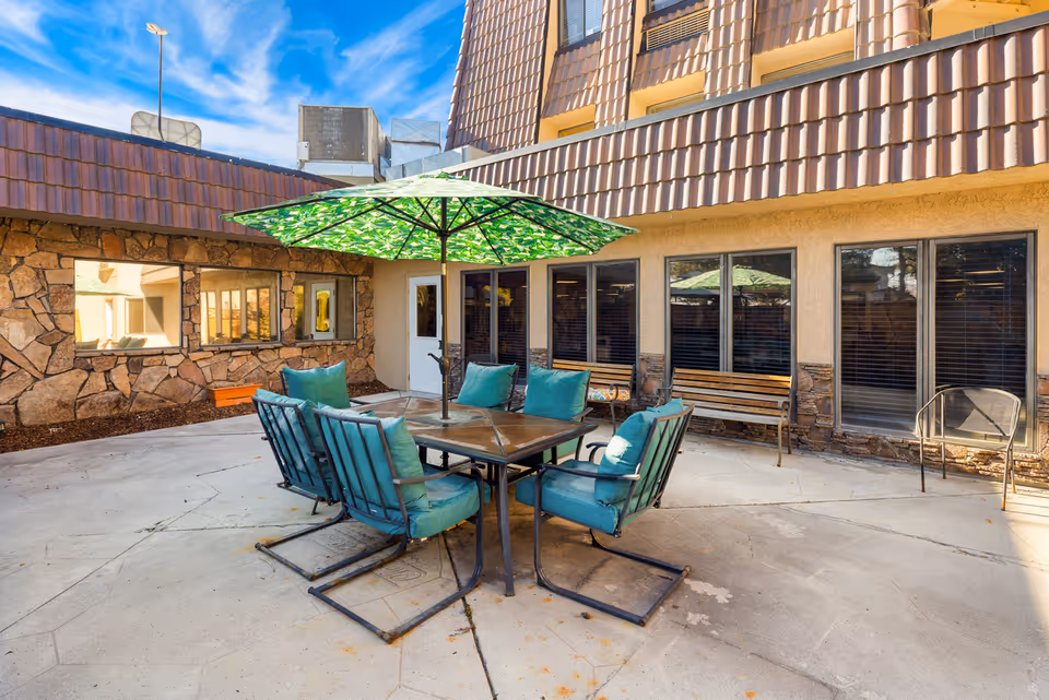 Outdoor courtyard patio with a table, teal cushioned chairs and a green umbrella in front of the building.