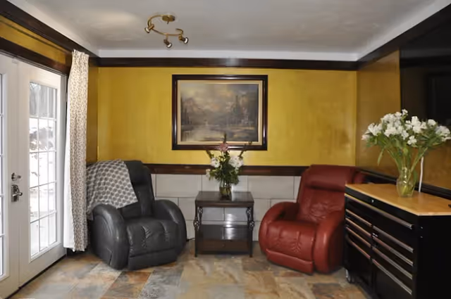 Small living area with two recliner chairs flanking a side table beneath a framed painting near French doors.