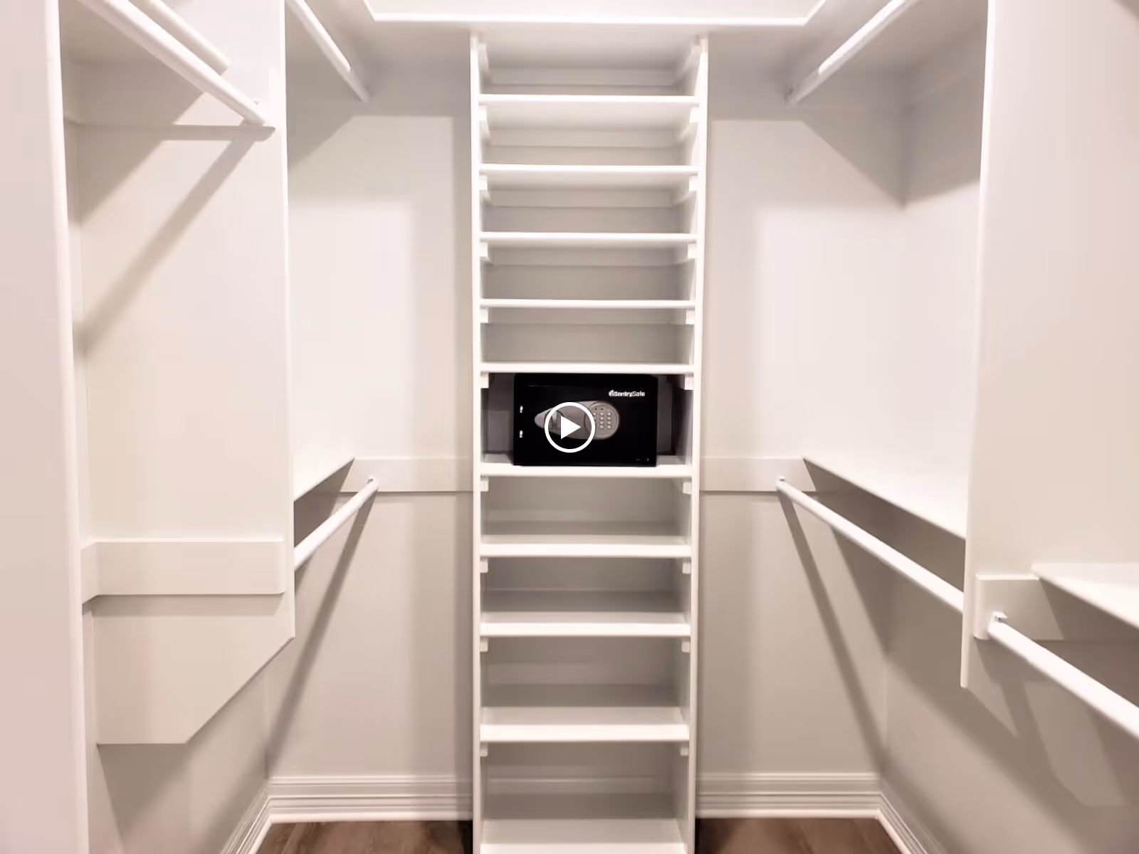 Empty walk-in closet with white shelving, hanging rods, and a small electronic safe on a center shelf.