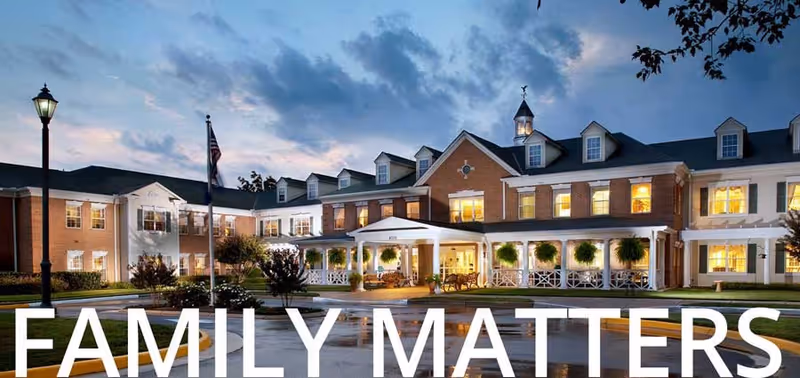 Front exterior of a senior living facility at dusk with lit windows, a covered entrance, landscaping, and the words "FAMILY MATTERS" across the bottom.