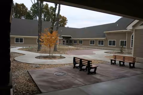 Exterior courtyard of a rehabilitation center with circular walkways, trees, and benches.
