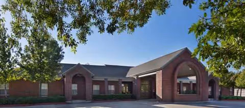 Braeswood Estates Senior Living building with arched entrance, trees framing the front exterior.