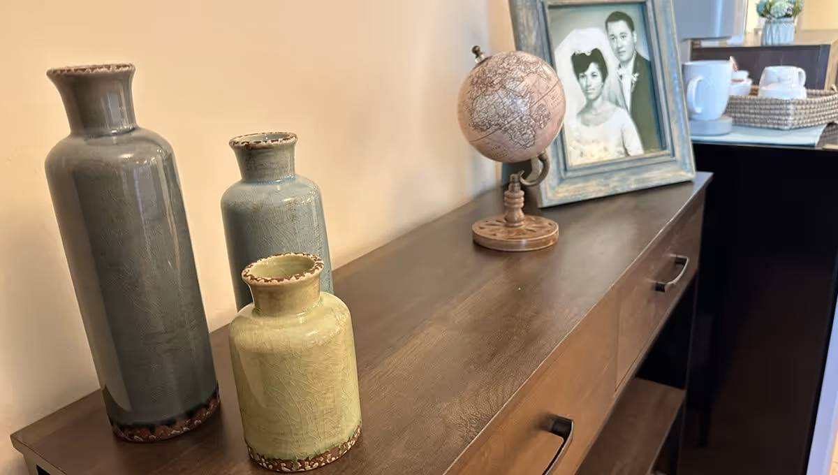 A wooden sideboard with three ceramic vases of varying sizes and colors on the left, a small decorative globe, and a framed black and white wedding photo on the right. In the background, there is a tray with white cups and a teapot.