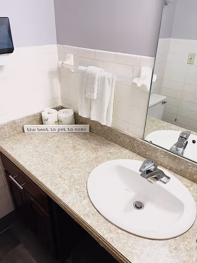 Bathroom vanity with a sink, faucet, countertop, mirror, towel on a rack, and a small sign that reads 'the best is yet to come'.
