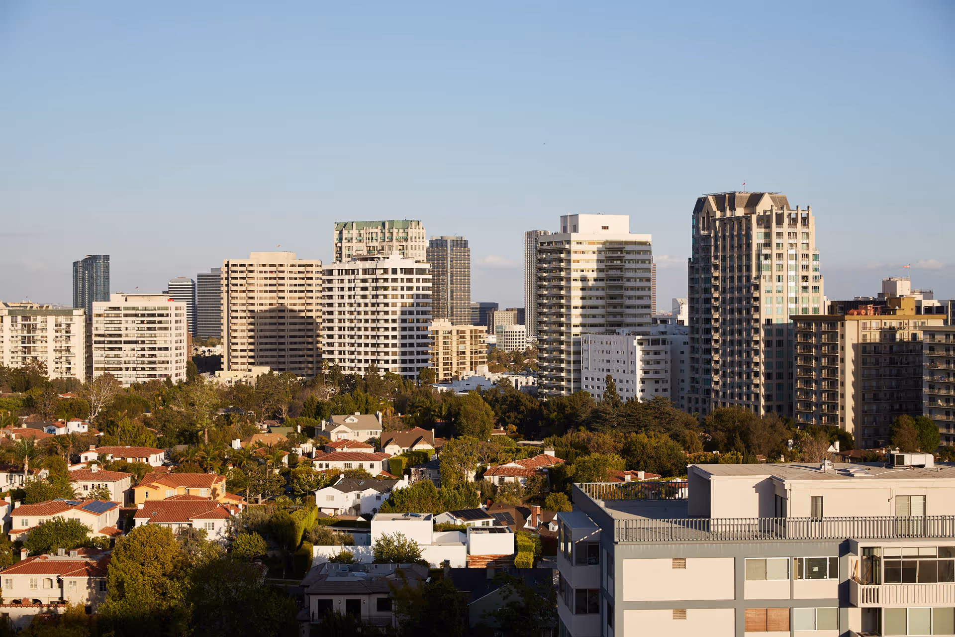 Cityscape showing low-rise houses in the foreground and mid- to high-rise apartment buildings under a clear sky.