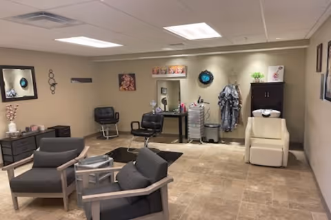 Spacious interior salon-style common room with styling chairs, a shampoo sink, seating area and wall decor.