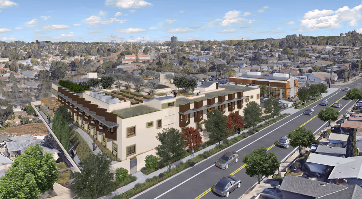 Aerial view of The Pavilion at Tecolote Canyon Senior Living facility showing a modern multi-story building with rooftop gardens and greenery. The building is surrounded by trees and a street with cars driving by. Residential houses and a cityscape are visible in the background under a partly cloudy sky.