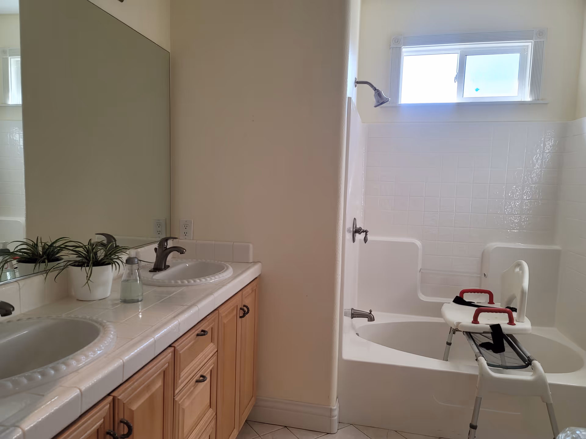 Bright bathroom with double sinks and mirror, and a bathtub fitted with a shower transfer chair.
