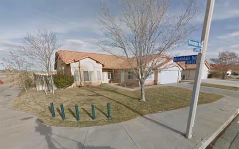 Exterior view of a single-story senior living facility with a small front yard and street sign.