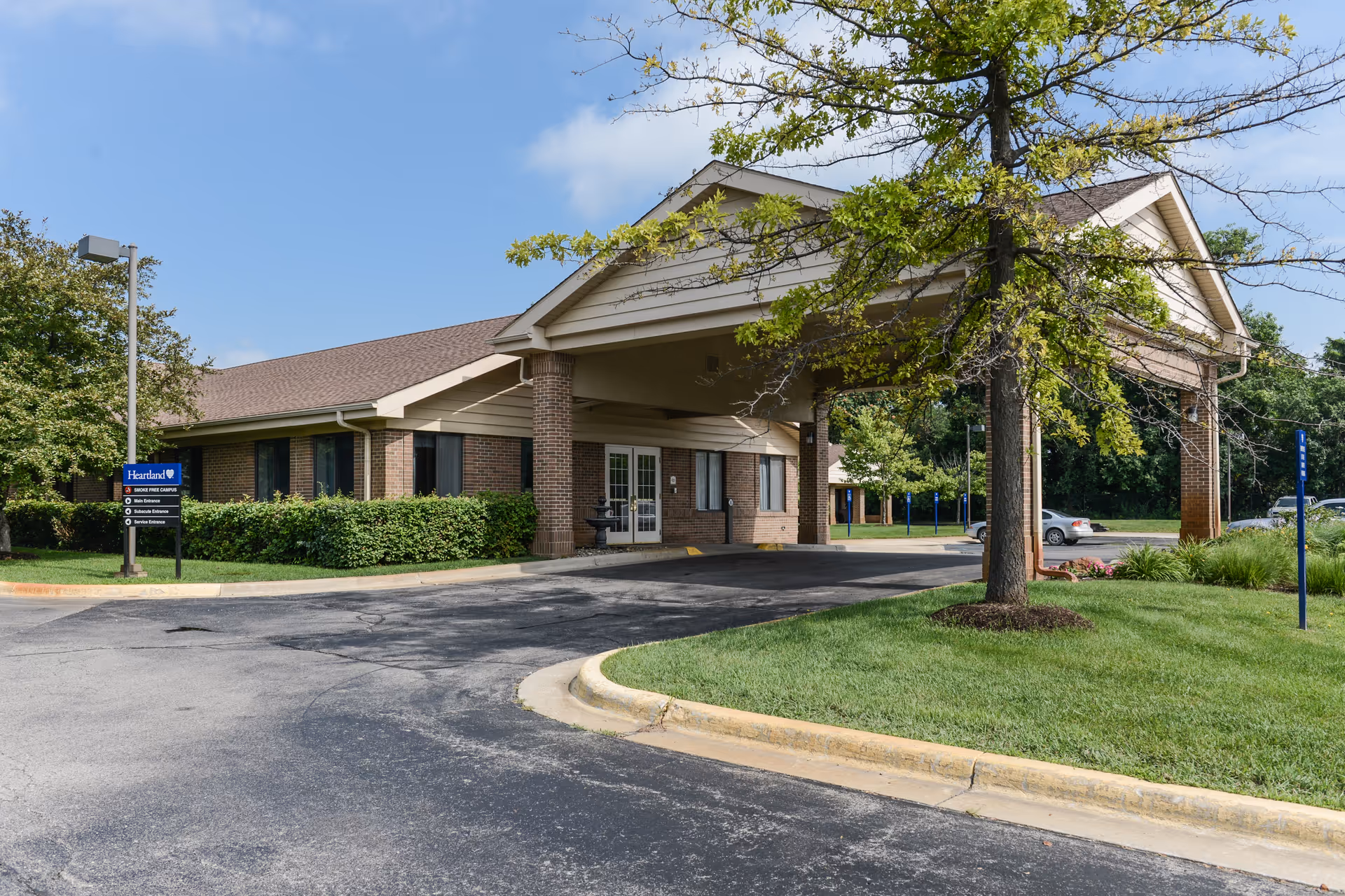 Exterior view of a brick senior living facility with a covered entrance, driveway, and well-kept landscaping.