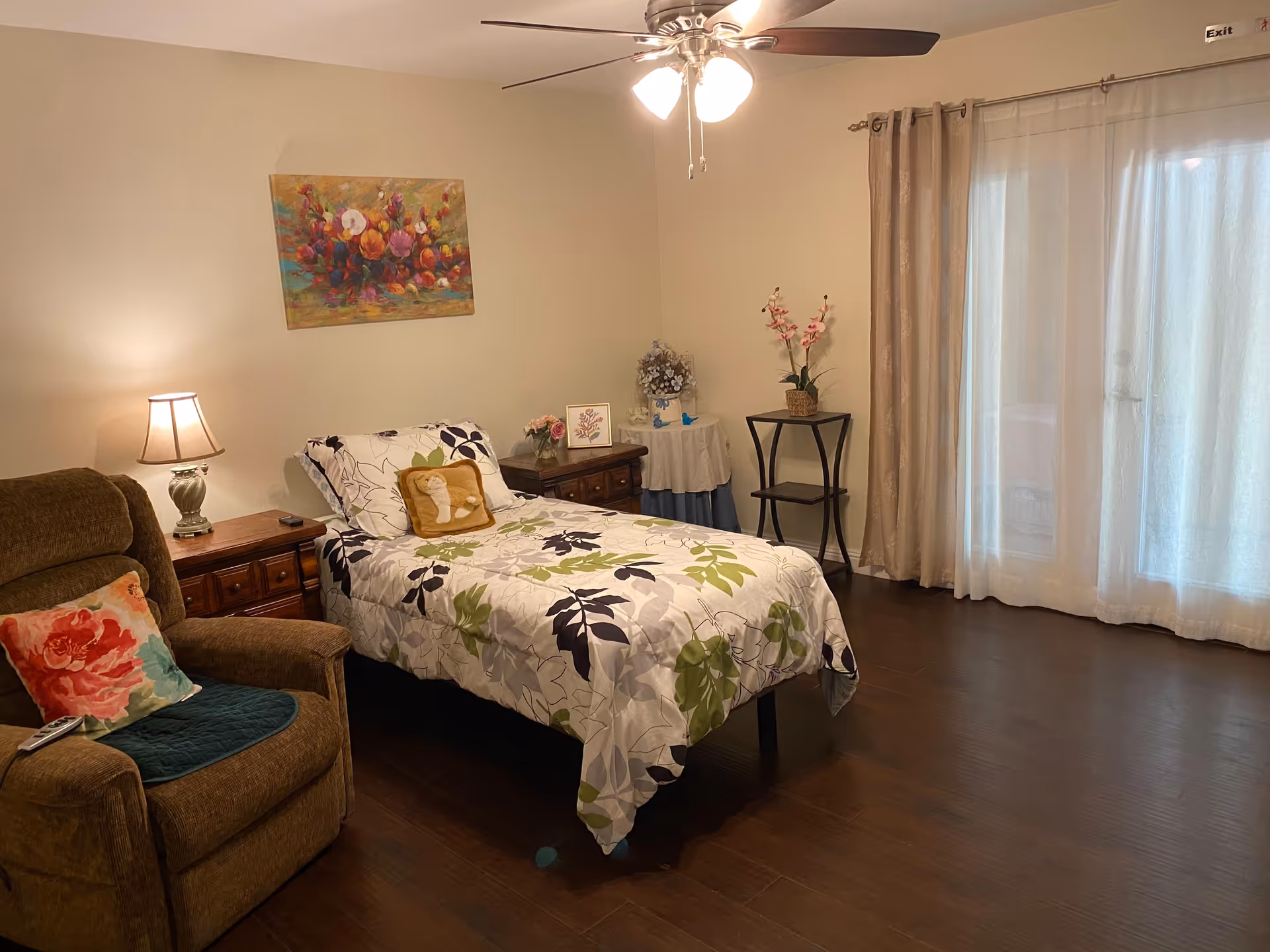 A cozy bedroom with a single bed, armchair, nightstand and sliding glass doors with curtains.