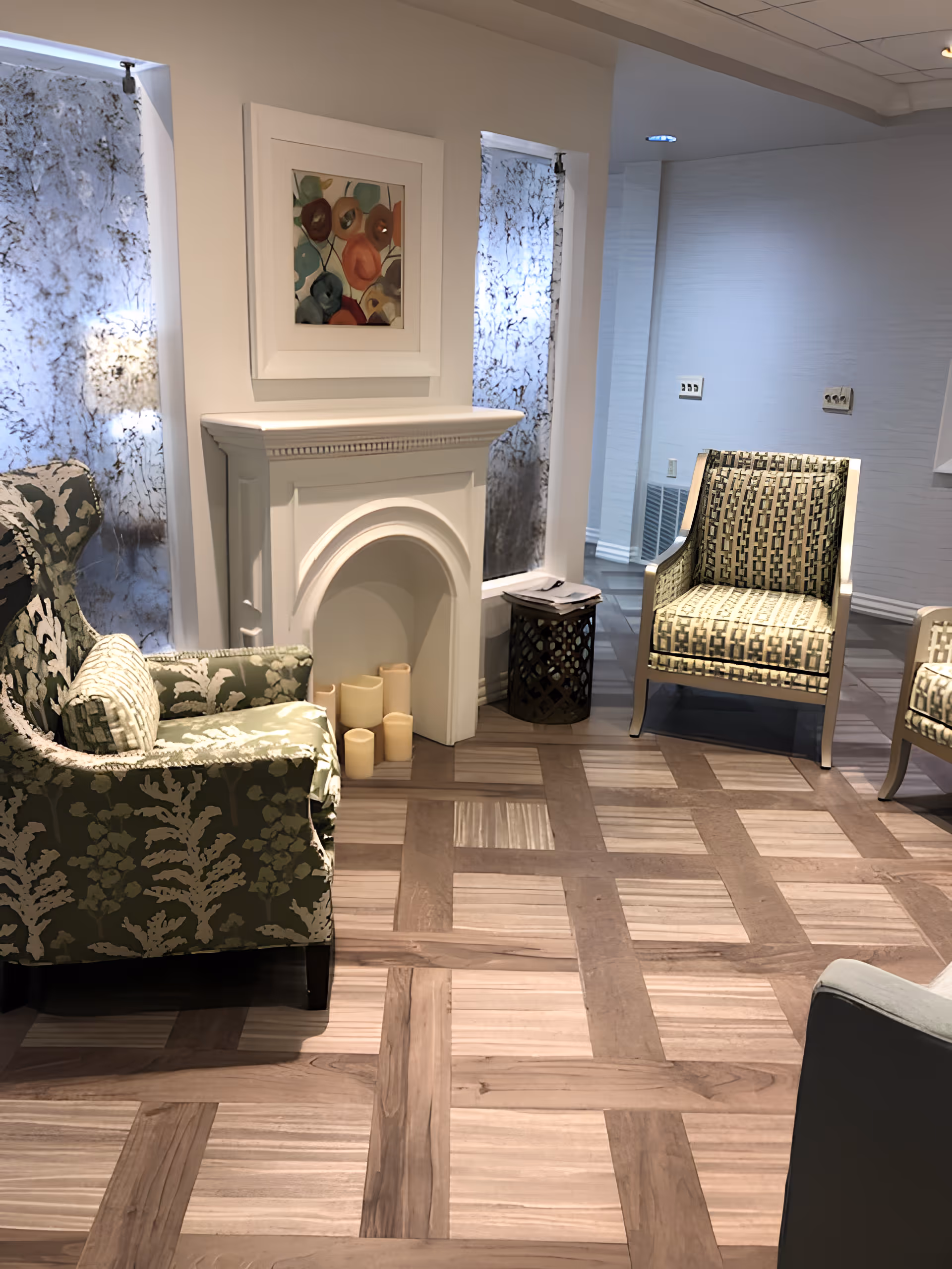 Cozy seating area with patterned armchairs, a decorative mantel, artwork, and parquet flooring.