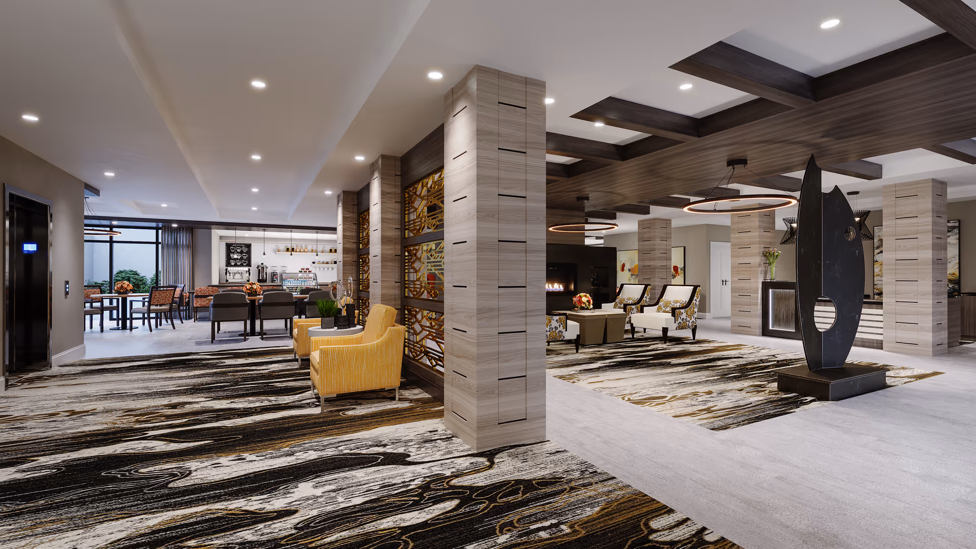 A spacious and modern senior living facility common area with patterned carpet, beige walls, and wooden ceiling beams. The room features comfortable seating including yellow armchairs and floral-patterned chairs around a coffee table near a fireplace. Decorative elements include a large abstract black sculpture and metal art panels on columns. In the background, there is a dining area with tables and chairs and a counter with coffee machines and other amenities.