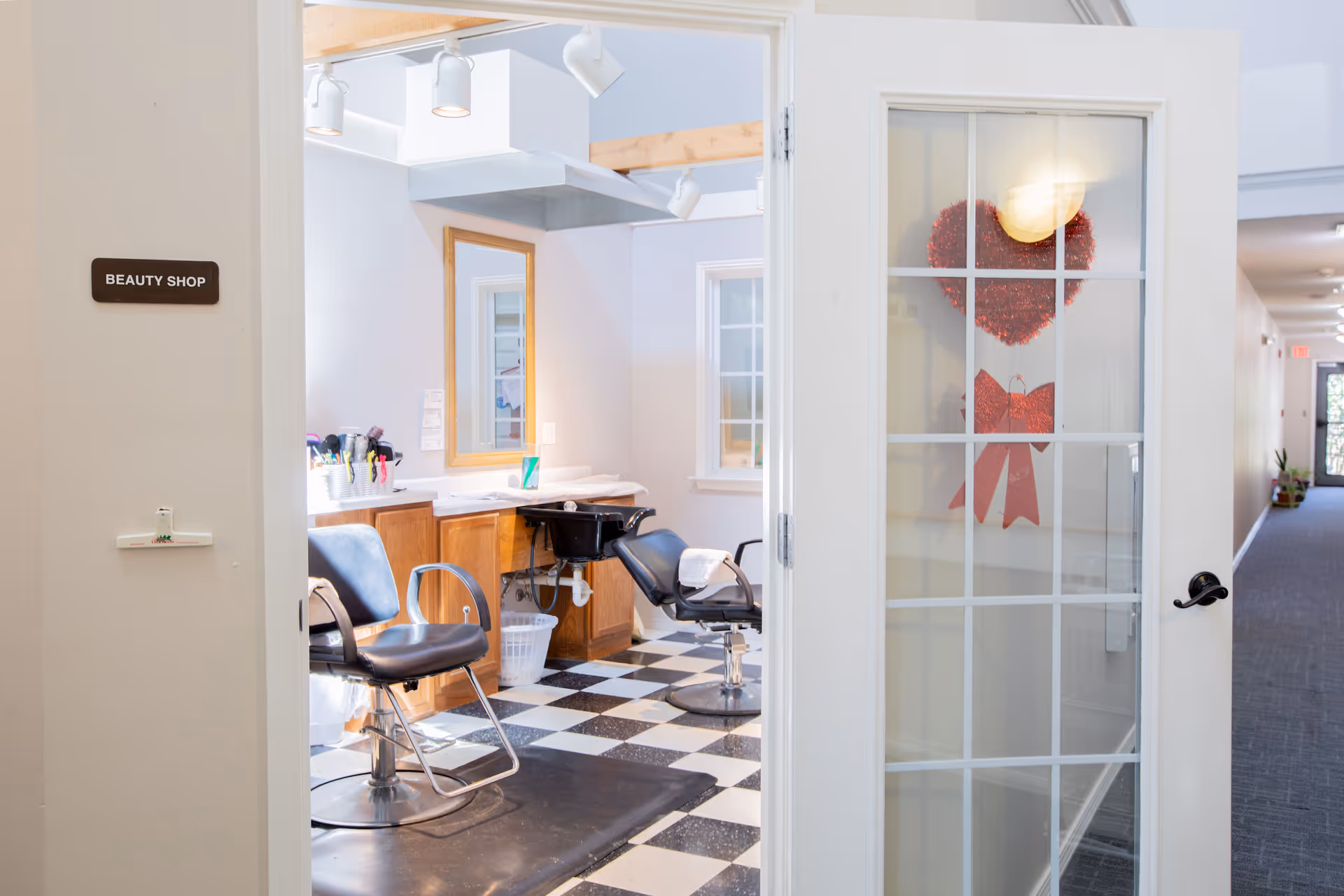 Open door revealing a small beauty shop with salon chairs, mirrors, and a black-and-white checkered floor.