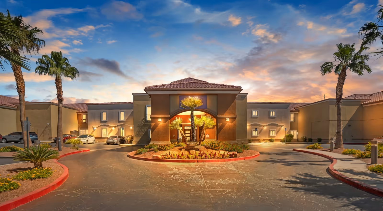 Senior living facility Acacia Springs exterior with palm trees and illuminated entrance at sunset.