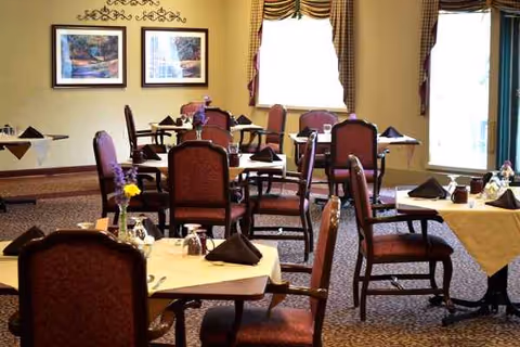 Senior living dining room with multiple tables, chairs, place settings, and floral centerpieces.