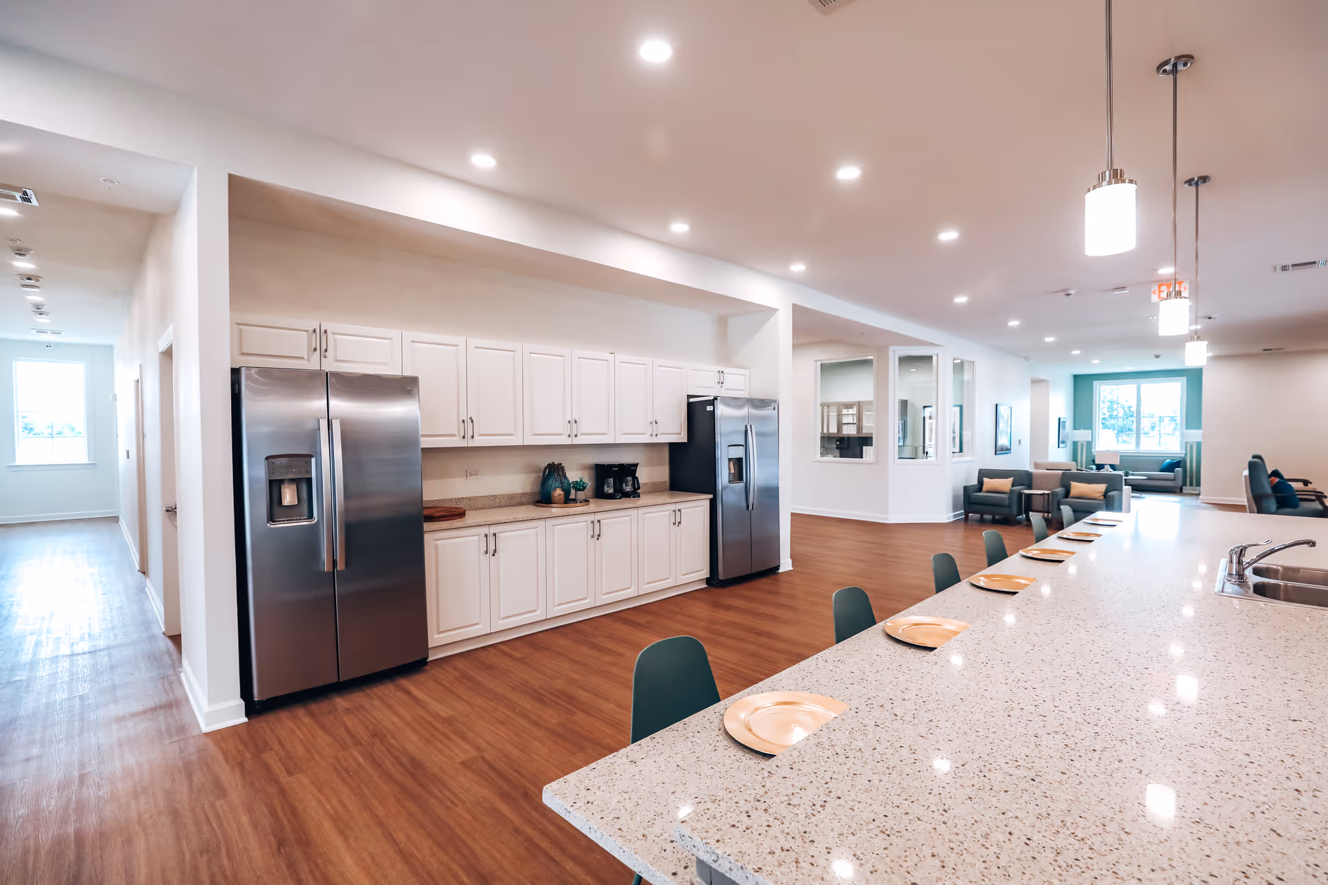 Bright open communal kitchen and lounge with a long speckled island, bar seating, stainless steel refrigerators and a seating area in the background.