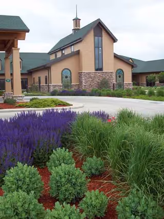 Facade of Heritage Estates senior living facility with landscaped purple flowers and greenery in foreground.
