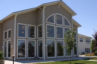 Exterior front view of a two-story senior living facility with large arched and rectangular windows and a landscaped lawn.