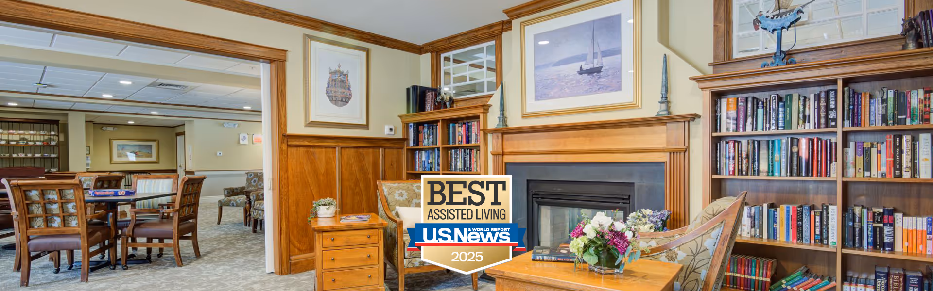 Cozy senior living common area with a fireplace, bookshelves, seating, and dining tables.