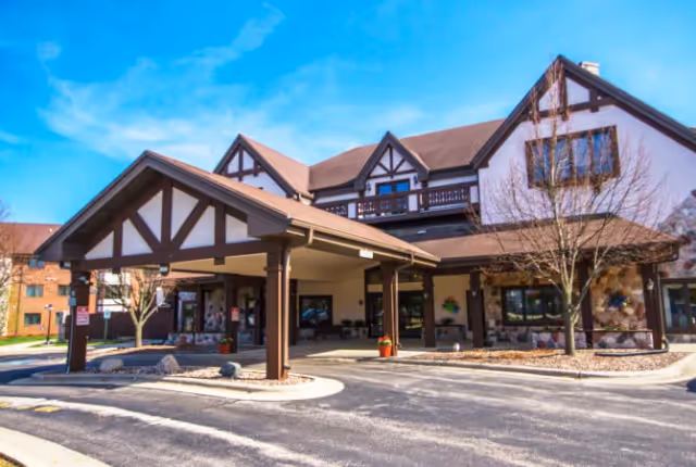 Front entrance of a Tudor-style senior living building with a covered porte-cochere and landscaped driveway.
