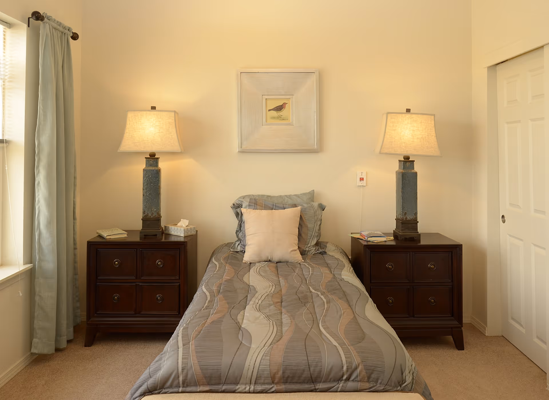 Small bedroom with a single bed centered between two dark wood nightstands topped with lamps and a framed bird picture on the wall.