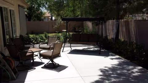 Outdoor patio with seating, a swing bench, and shaded trees along a fenced yard.