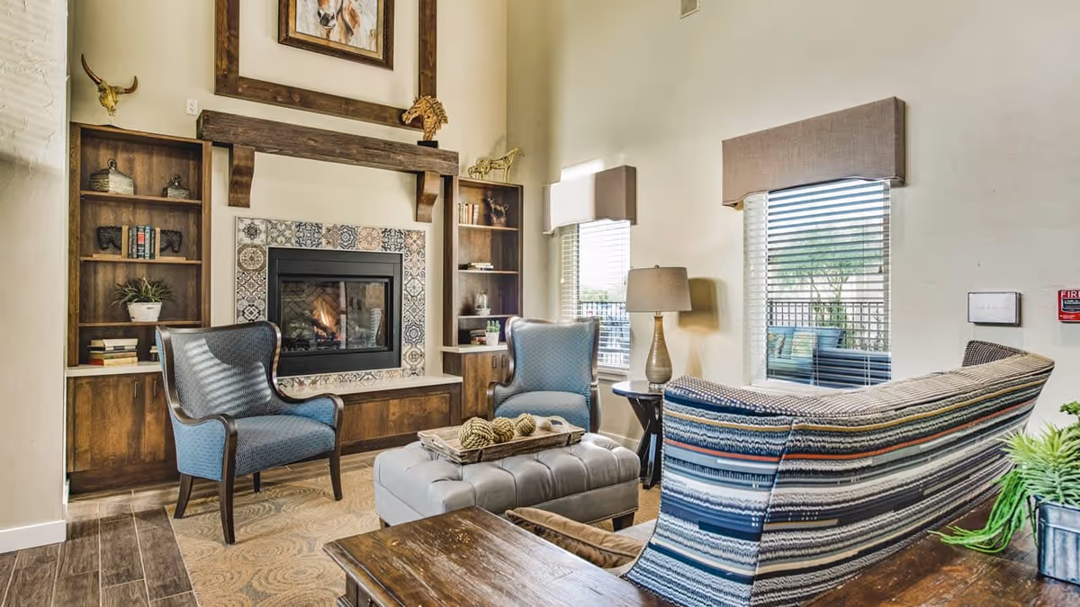 Cozy living room with a tiled fireplace flanked by built-in bookshelves, two armchairs, a striped sofa, and a tufted ottoman.