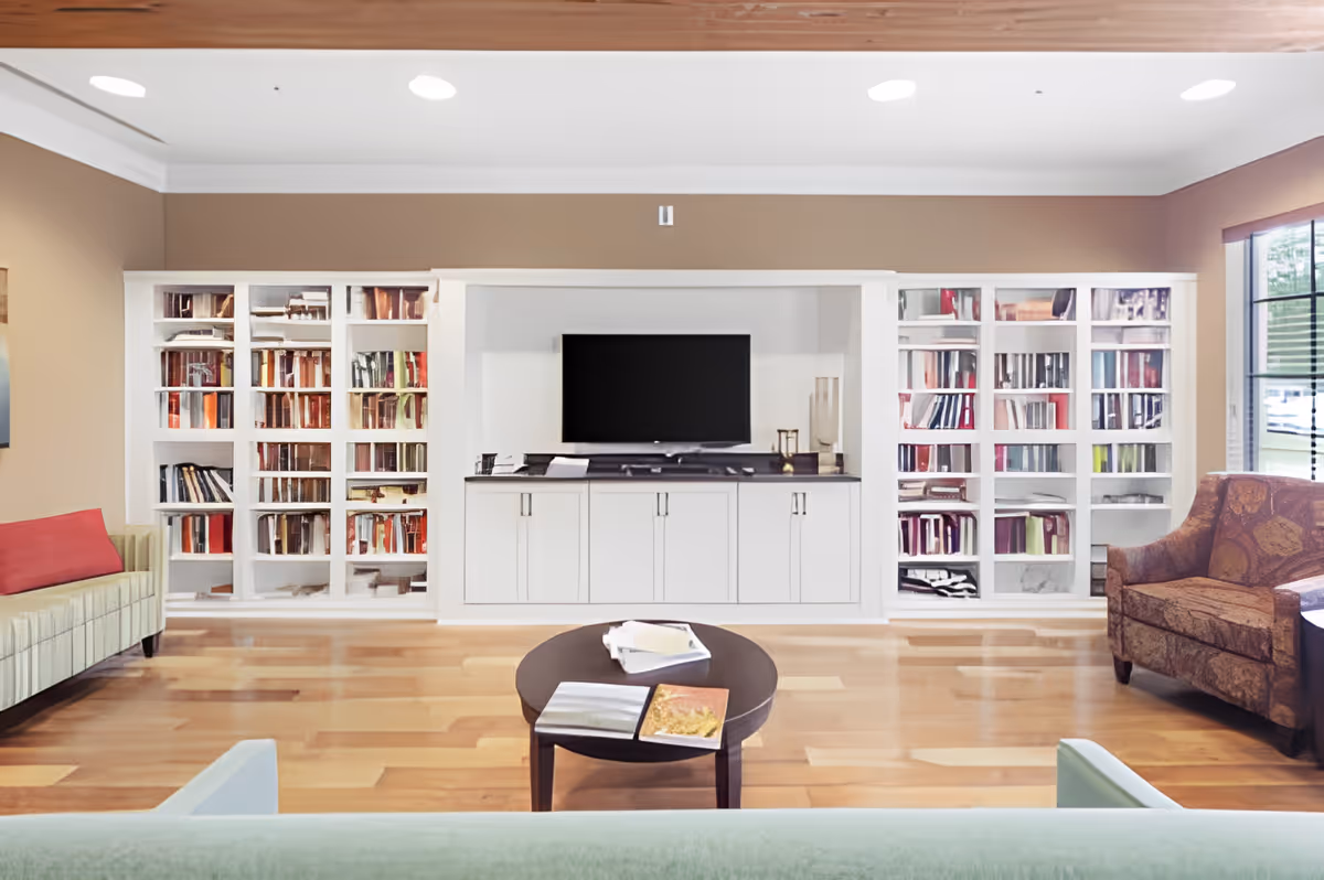 Bright communal living room with built-in white bookshelves and a TV, a central coffee table, and assorted seating.