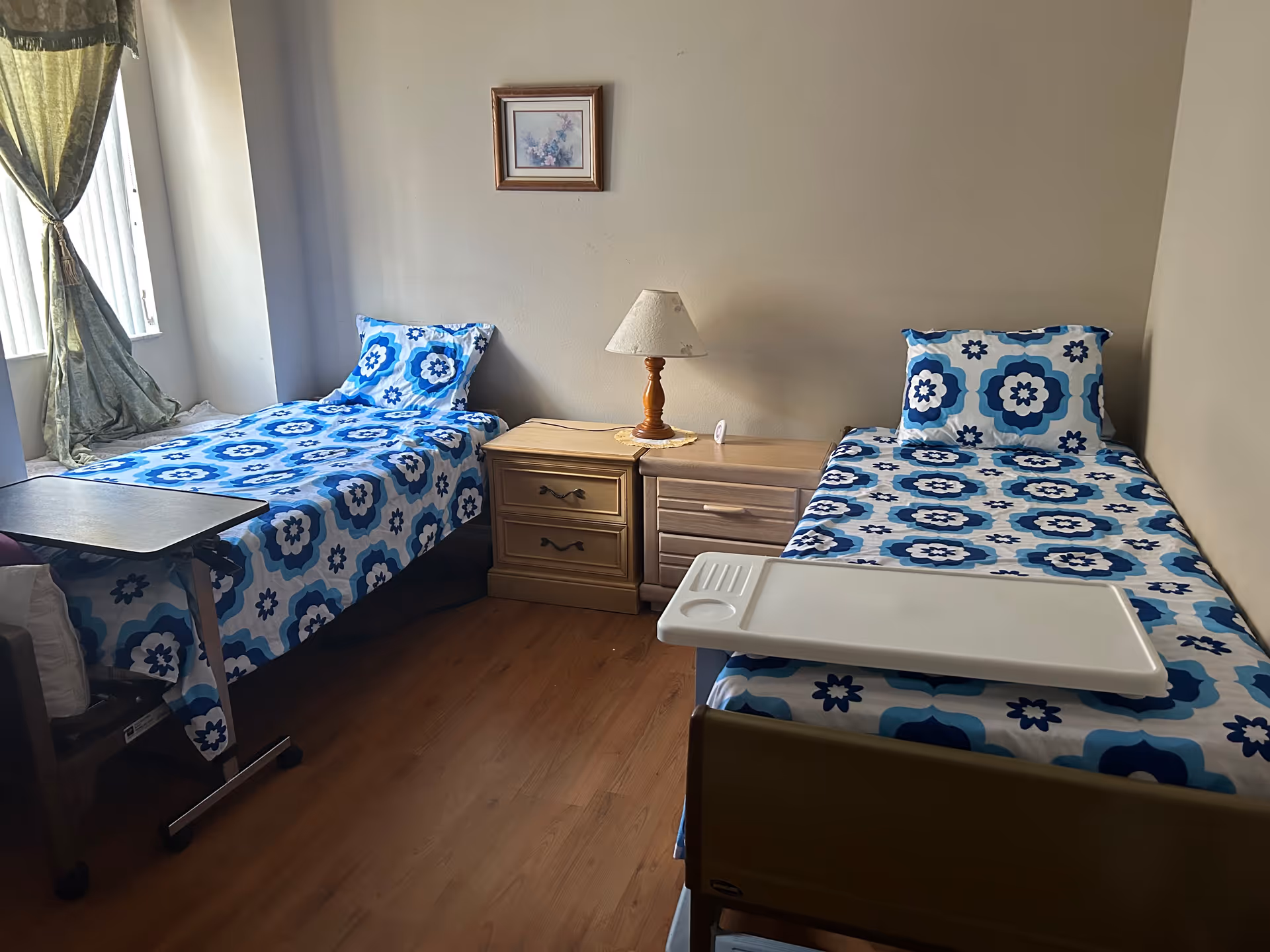 Two single beds with blue floral bedding, nightstand, and lamp in a shared bedroom.