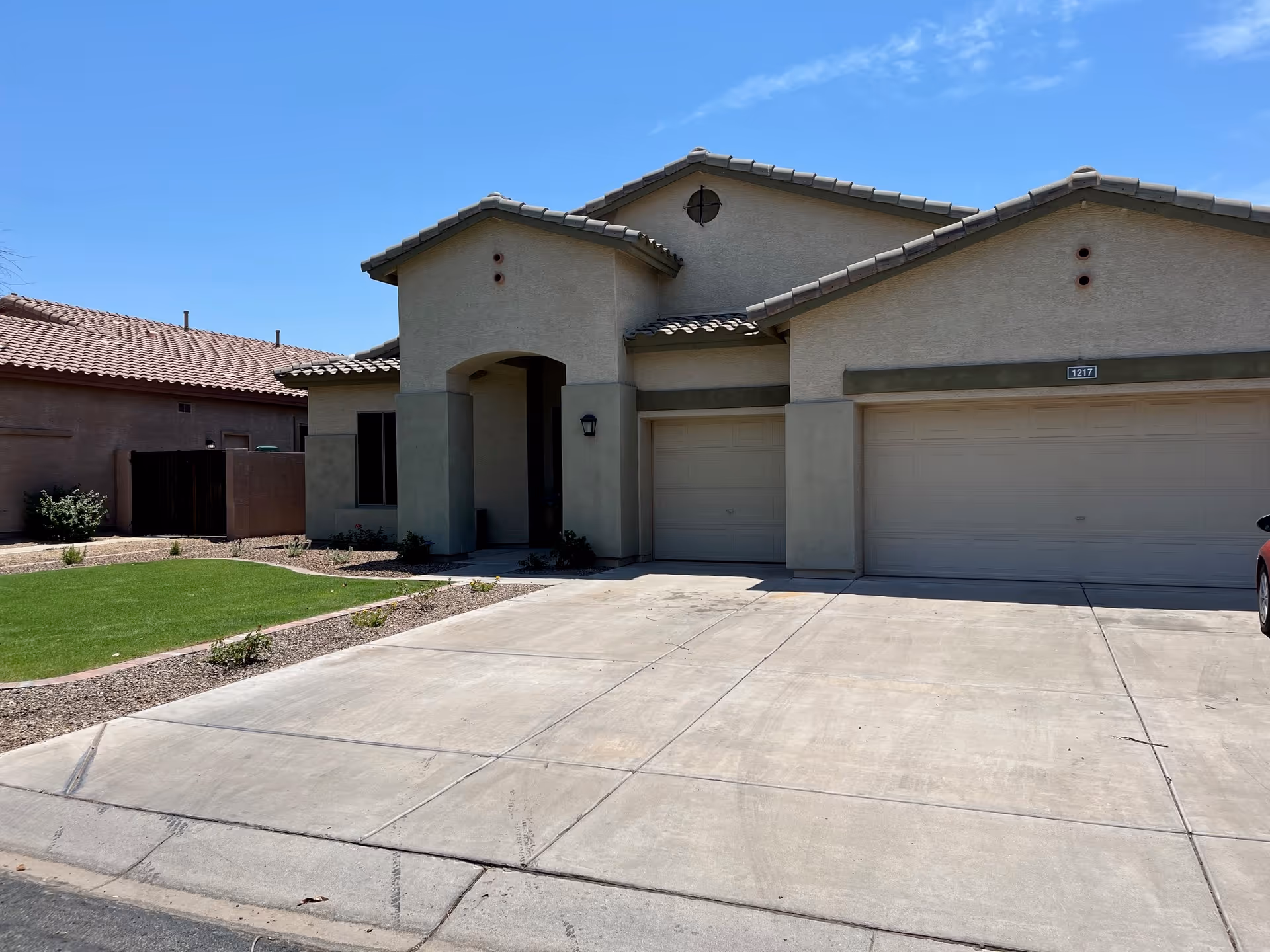 Front exterior of a stucco single-family home with a three-car garage and driveway under a clear blue sky.