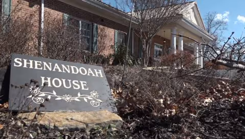 Front exterior of Shenandoah House with a sign and leafless shrubs at entry.