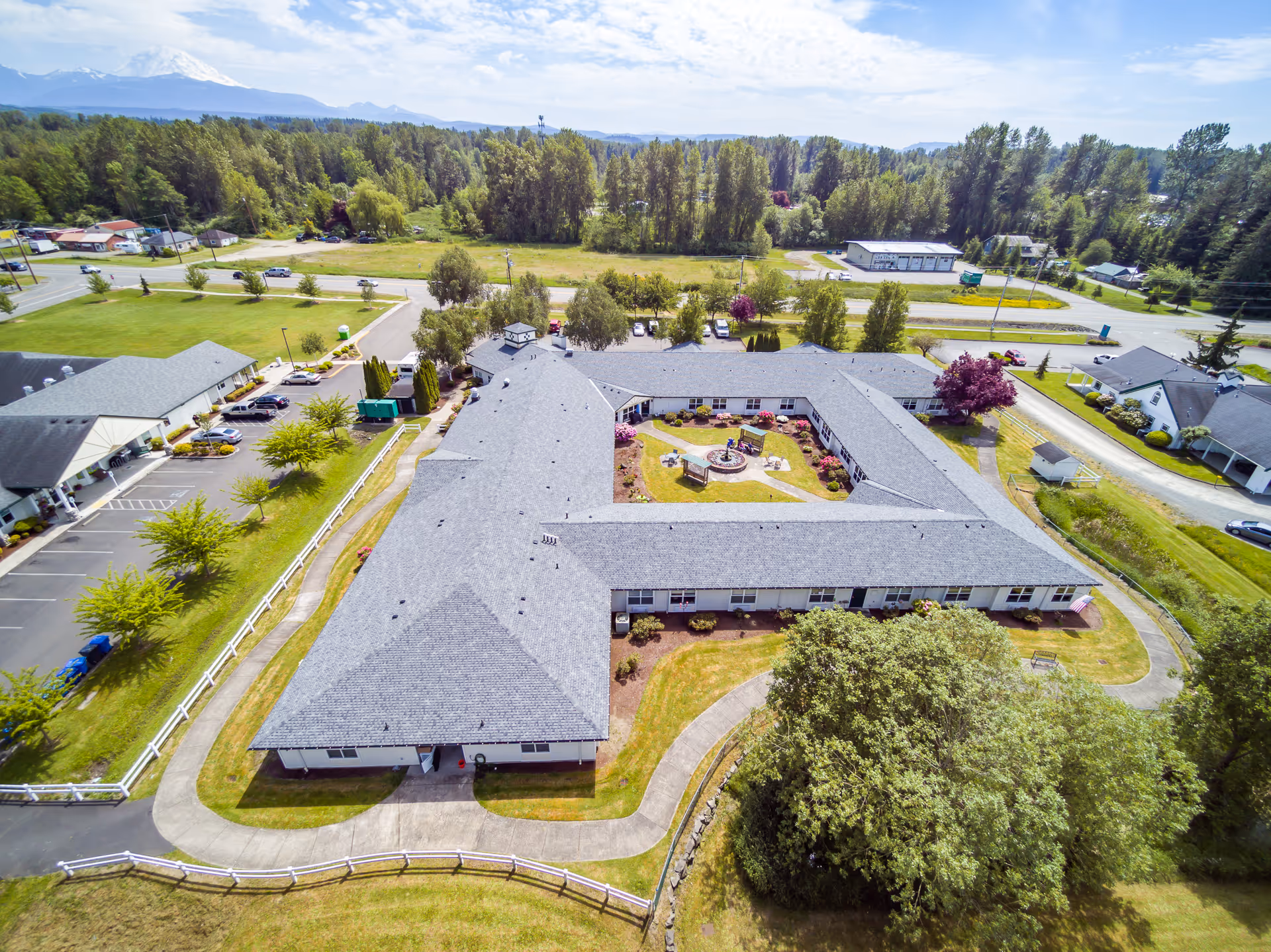 Aerial view of a single-story assisted living facility arranged around a landscaped central courtyard with surrounding lawns, parking, and trees.