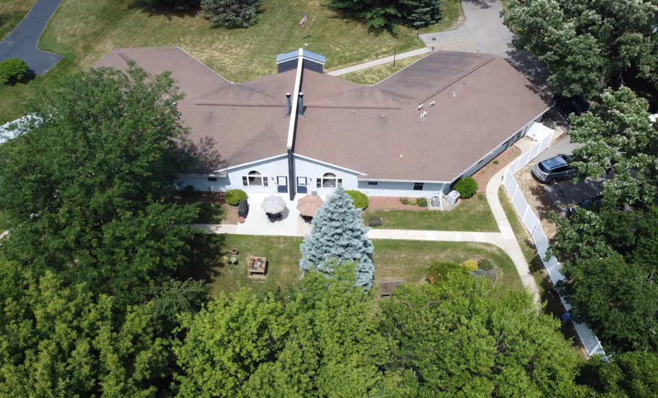 Aerial view of a single-story memory care building with a central entrance, patio area, walkways, and surrounding trees.