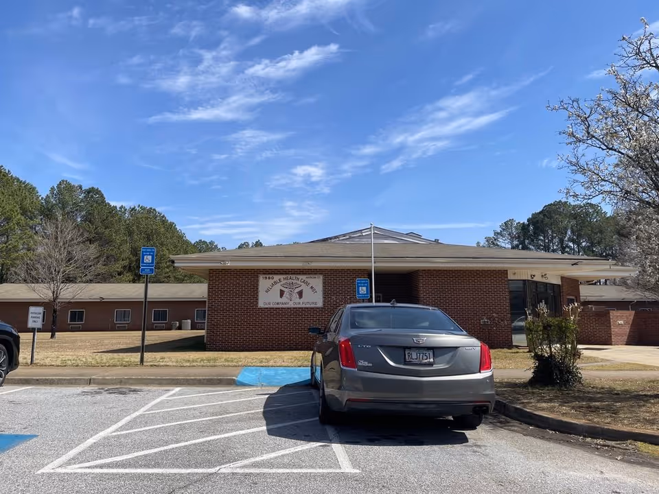 Front exterior of a single-story brick senior health and rehab building with a parked car and accessible parking spaces.