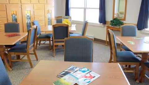 Senior living dining room with wood tables, blue chairs, and magazines
