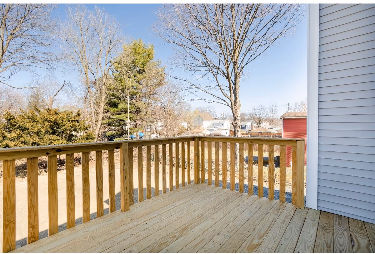 Wooden deck with a railing overlooking a yard, trees, and neighboring houses.