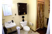 Small bathroom with a wall-mounted sink and mirror, a toilet beneath a dark wall cabinet, a patterned shower curtain, and a towel rack.
