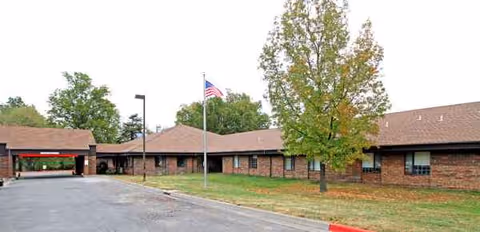 Exterior of a brick, single-story facility with a parking lot, flagpole, and trees.